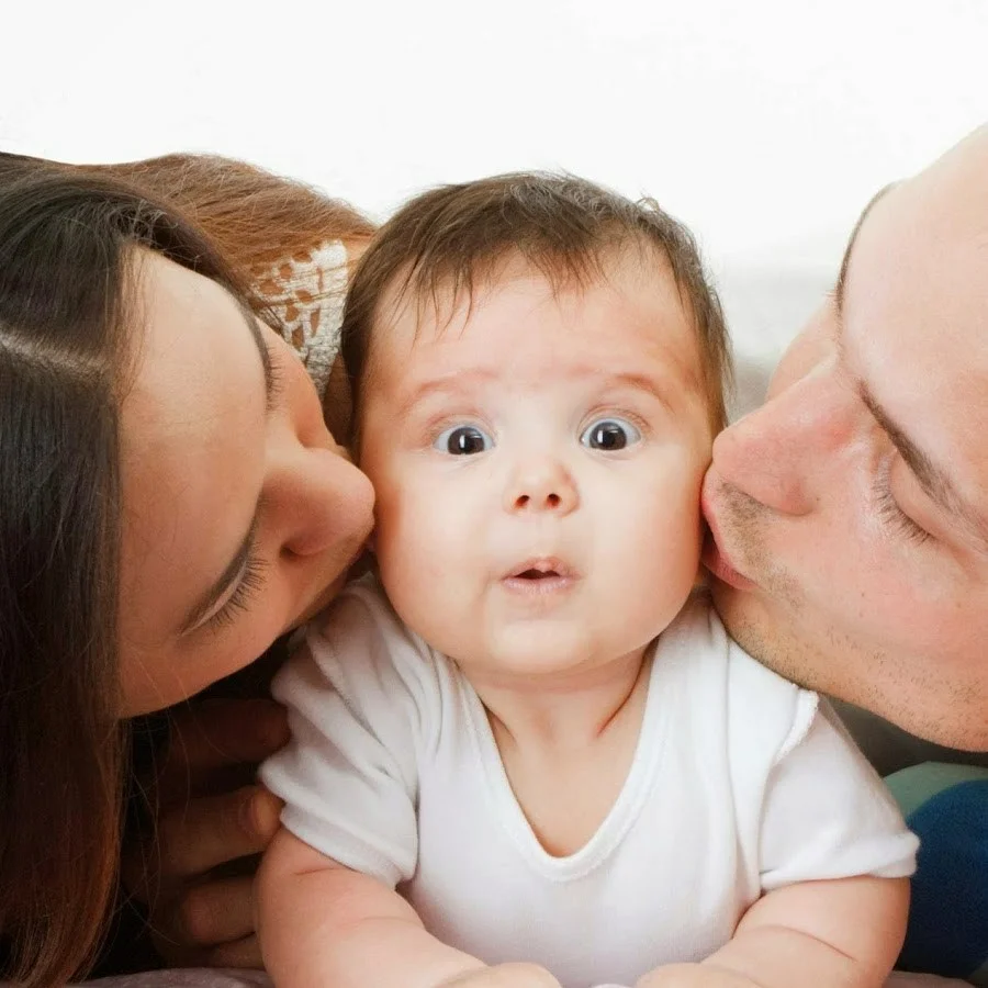 two parents kissing a little baby